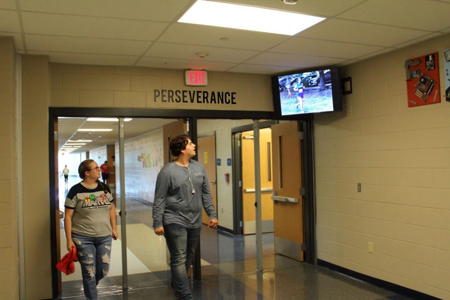Students look at a picture from a cross country meet as they walk by a new TV in the upstairs hallway. The new TVs display pictures and videos from recent events. 