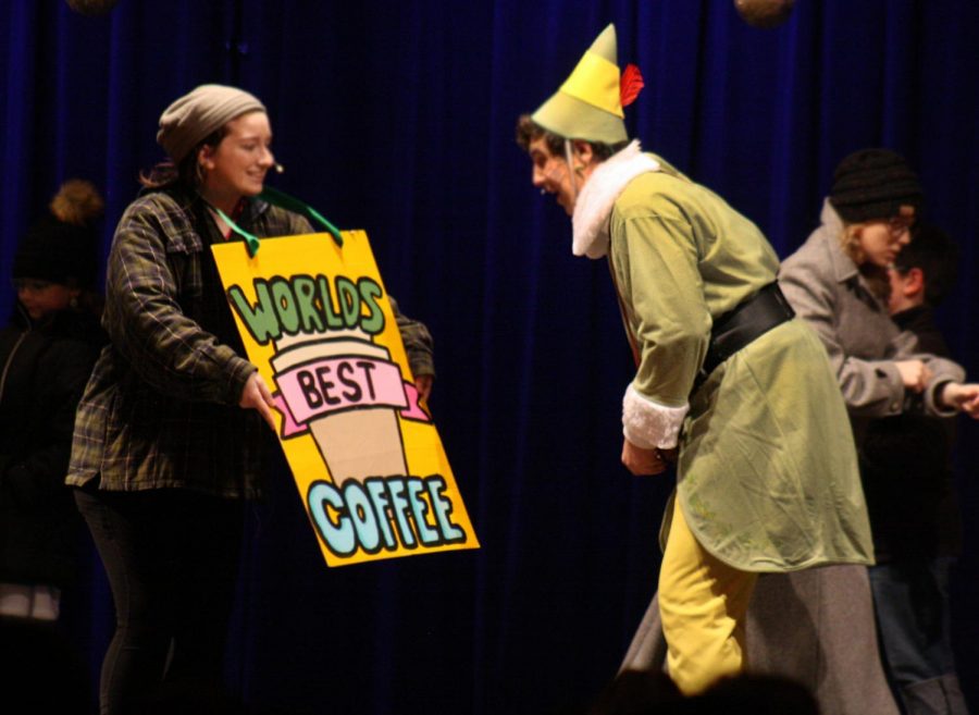 Freshman Kaitie McClendon holds a sign in front of junior Cole Wheeler during Elf The Musical. 