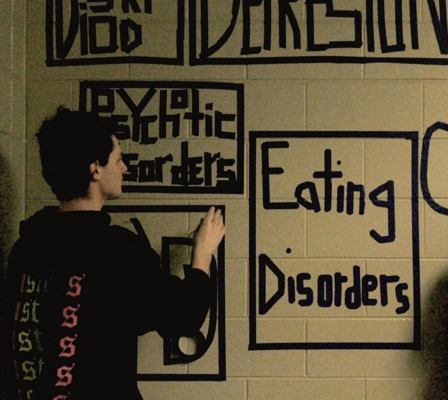 Junior Cole Babb creates a tape mural in the hall for art class. It is part of a series of murals about teen social issues. This one depicts mental illness.