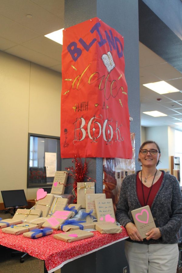 Assistant librarian Sarah Cimino holds one of the wrapped books for Blind Date with a Book. Student library aides wrapped and decorated the books and created the sign.  