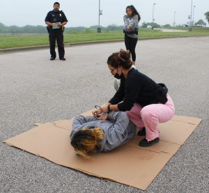 Senior Victoria  Garza puts handcuffs on sophomore DJ Ramirez during the felony traffic stop simulation for the tactical competition April 23. Sophomore Amore Zapata assists in the the background while Officer Hernandez monitors and judges for the contest. 