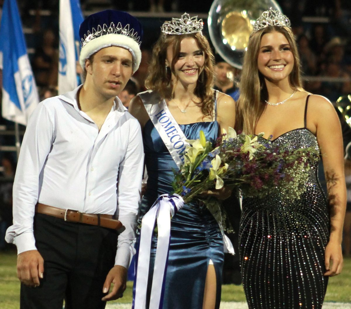 Homecoming King Jimmy Mcanally, Homecoming Queen Hailey Palmer, and former Homecoming Queen Kenzie Roberts posing on the field.