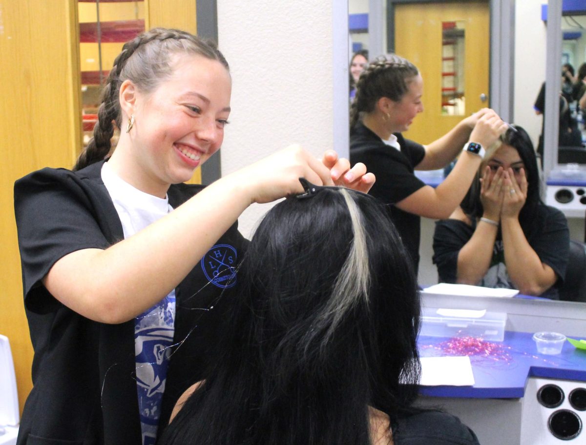 Junior Lilly Dibattiste applies hair tinsel for sophomore Isabella Jurado Sept. 5.